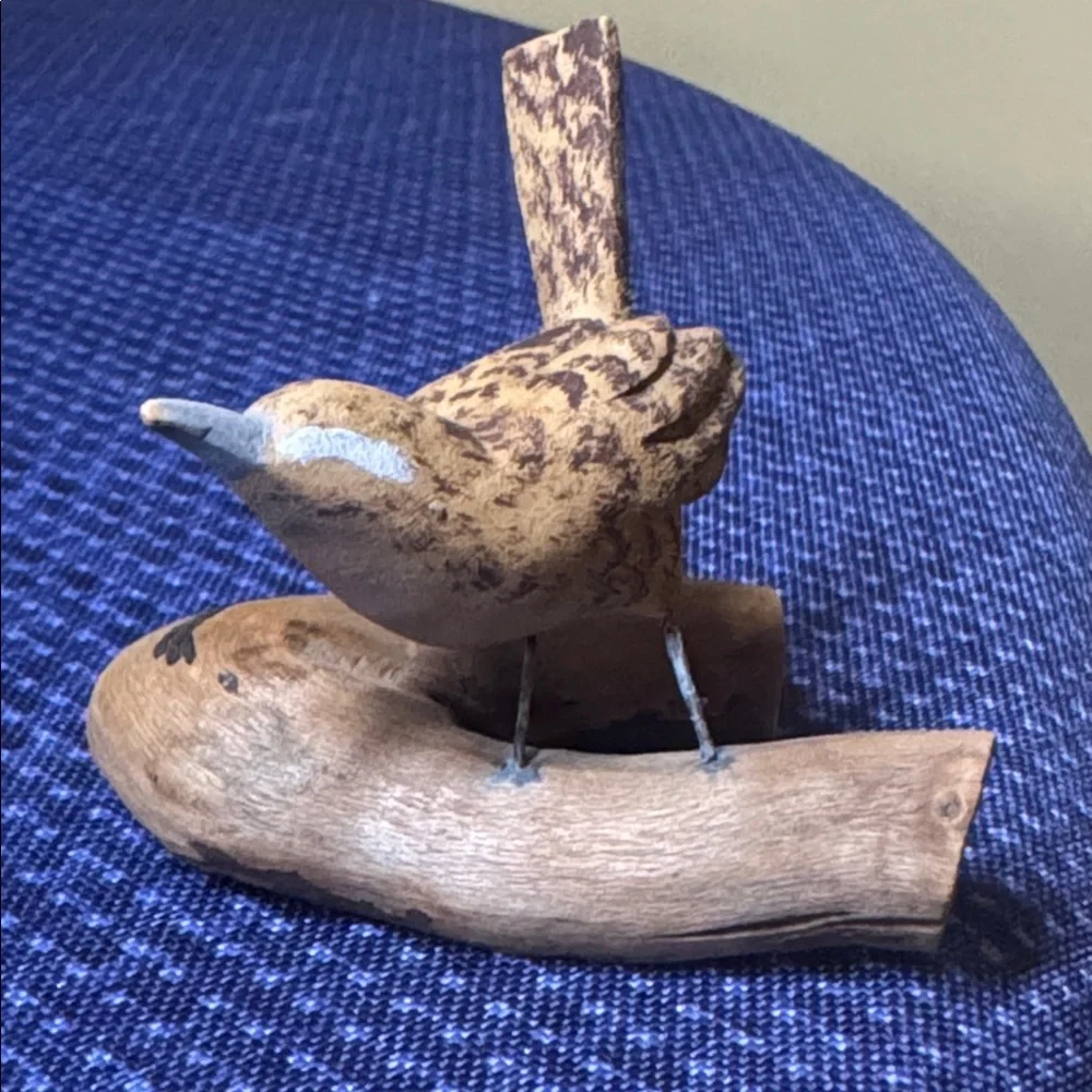 Hand carved wooden bird sculpture perched on a piece of natural wood signed